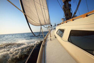 Güneşli bir günde beyaz bir yat denize açılıyor. Güverteden pruva ve yelkenlere kadar yakın çekim. Dalgalar ve su sıçramaları. Britanya, Fransa