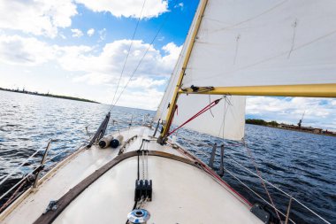 Açık bir günde beyaz bir yat gezintisi. Güverteden pruvaya ve yelkenlere bir manzara. Dalgalar ve su sıçramaları. Baltık Denizi, Letonya