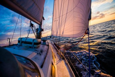 White yacht sailing at sunset. A view from the deck to the bow and sails. Waves and clouds. Baltic sea clipart