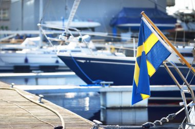 Sailing boats moored to a pier after winterization in winter. Flag of Sweden close-up. Port of Riga, Latvia clipart