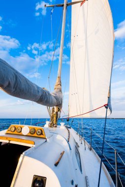 Gün batımında durgun suda yüzen beyaz bir yat. Güverteden pruvaya, direğe ve yelkenlere bir manzara. Şaşırtıcı bulut manzarası. Doğal ayna. Spor ve eğlence teması. Baltık Denizi, Letonya