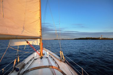 Gün batımında yelkenli tekneyle açılacak. Güverteden pruvaya ve yelkenlere bir manzara. Dalgalar ve su sıçramaları. Baltık Denizi, Letonya