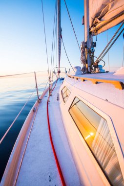 Sakin su. Günbatımında beyaz yelkenli tekneyle denize açılacak. Güverteden pruvaya, direğe ve yelkenlere bir manzara. Baltık Denizi, Letonya