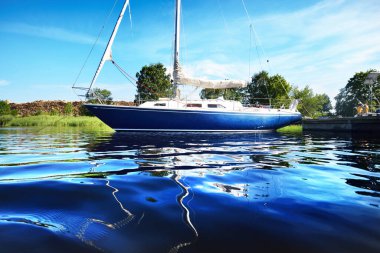 Mavi yat bir rıhtıma demirlemiş, sudan bir manzara. Açık mavi gökyüzü. Daugava Nehri, Riga Limanı, Letonya
