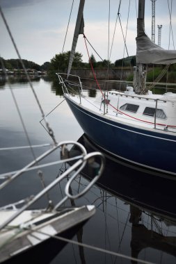 Mavi şalopalı yat iskeleye demirli, yakın plan. Fırtına gökyüzü. Suda yansıma. Riga Limanı, Letonya