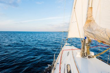 Gün batımında durgun suda yüzen beyaz bir yat. Güverteden pruvaya, direğe ve yelkenlere bir manzara. Şaşırtıcı bulut manzarası. Doğal ayna. Spor ve eğlence teması. Baltık Denizi, Letonya