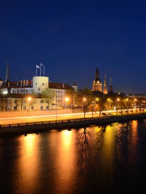 Letonya 'nın Riga kentinin aydınlık manzarası, gece vakti Daugava nehir geçidinde. Karanlık şehir manzarası. Seyahat yerleri, işaretler, turizm, kültür.