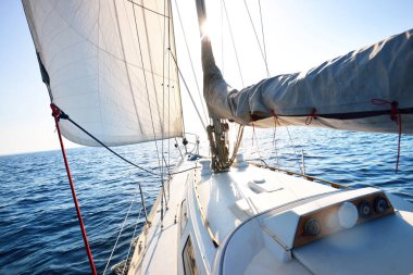 Güneşli bir günde beyaz bir yat denize açılıyor. Güverteden pruva ve yelkenlere kadar yakın çekim. Dalgalar ve su sıçramaları. Britanya, Fransa