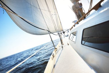 Güneşli bir yaz gününde beyaz bir yat denize açılıyor. Güverteden pruva ve yelkenlere kadar yakın çekim. Dalgalar ve su sıçramaları. Açık mavi gökyüzü. Baltık Denizi, İsveç. Ulaşım, spor, eğlence aktivitesi