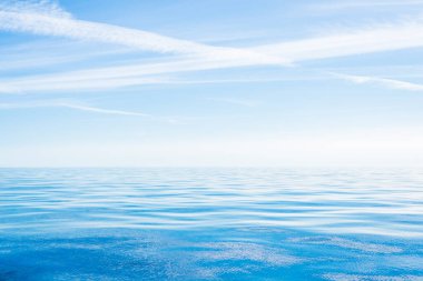 Deniz suyu dokusu. Açık mavi gökyüzü, beyaz bulutlar ve uçak izleri. Sudaki yansımalar. Baltık Denizi, Estonya