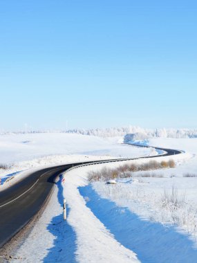 Karla kaplı tarlalar, ormanlar, köyler boyunca uzanan boş S şeklindeki otoyolun manzarası. Kırsal kesimde kış manzarası. Seyahat, Noel tatili, lojistik, tehlikeli sürüş, off-road, ulaşım