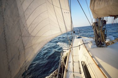 Güneşli bir günde beyaz bir yat denize açılıyor. Güverteden pruva ve yelkenlere kadar yakın çekim. Dalgalar ve su sıçramaları. Britanya, Fransa