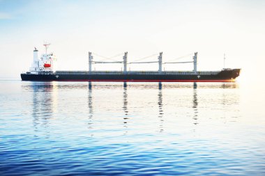 Gün batımında büyük bir yük vinci gemisi. Akşam bulutları ve parlak güneş ışığı. Baltık Denizi, Letonya