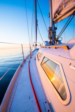 Sakin su. Günbatımında beyaz yelkenli tekneyle denize açılacak. Güverteden pruvaya, direğe ve yelkenlere bir manzara. Baltık Denizi, Letonya