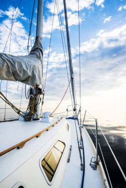 Gün batımında durgun suda yüzen beyaz bir yat. Güverteden pruvaya, direğe ve yelkenlere bir manzara. Şaşırtıcı bulut manzarası. Doğal ayna. Spor ve eğlence teması. Baltık Denizi, Letonya