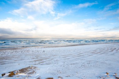 Gün batımında karla kaplı deniz manzarası ve Baltık denizi. Açık mavi gökyüzü, akşam bulutları.