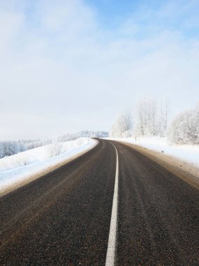 Karla kaplı tarlalar, ormanlar, köyler boyunca uzanan boş S şeklindeki otoyolun manzarası. Kırsal kesimde kış manzarası. Seyahat, Noel tatili, lojistik, tehlikeli sürüş, off-road, ulaşım