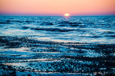 Renkli gün batımı. Güneşli bir kış gününde, karla kaplı deniz kıyısında. Letonya, Baltık Denizi üzerinde soğuk dalgalar