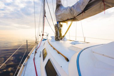 Gün batımında durgun suda yüzen beyaz bir yat. Güverteden pruvaya, direğe ve yelkenlere bir manzara. Şaşırtıcı bulut manzarası. Doğal ayna. Spor ve eğlence teması. Baltık Denizi, Letonya