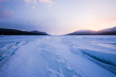 Gün batımında Kandalaksha Körfezi 'nin buz basıncı sırtı. Renkli akşam bulutları. Arka planda Kola Yarımadası 'nın dağları ve kozalaklı ormanları var. Beyaz deniz, Kutup dairesi, Karelia, Rusya