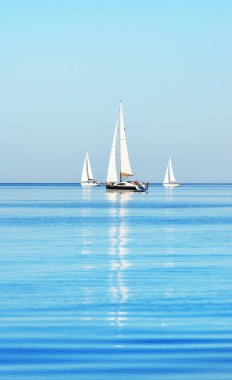 Açık ve güneşli bir günde Akdeniz 'de yelkenli dolu yatlar. Beyaz bulutlu mavi gökyüzü, suda yansımalar.