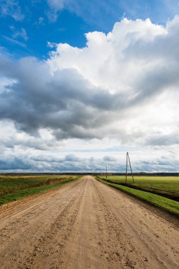 Sonbahar. Boş toprak yolun üzerindeki fırtına bulutları. Arka planda tarım alanları ve orman var. Sıcak akşam güneşi. Baltık Denizi, Garciems, Letonya