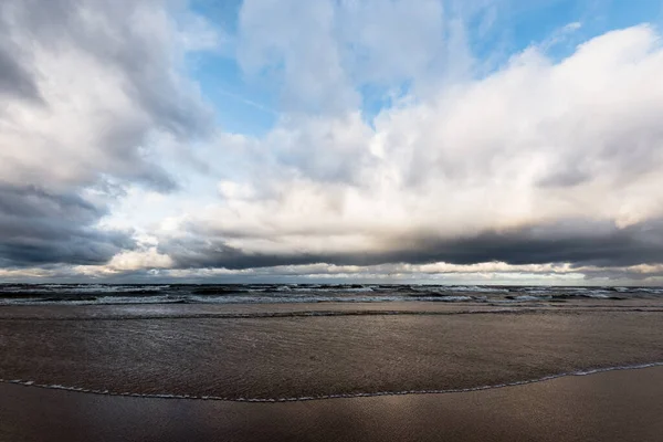 Autumn. Storm clouds above the sea. Waves and water splashes. Warm evening sunlight. Baltic sea, Garciems, Latvia