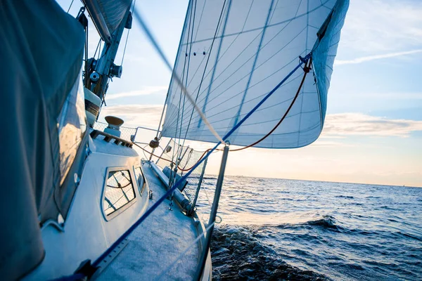 stock image White yacht sailing at sunset. A view from the deck to the bow and sails. Waves and clouds. Baltic sea