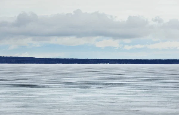 A view of the frozen Onega lake after a blizzard. Forest in the background. Dramatic evening sky. Stunning cloudscape. Karelia, Russia