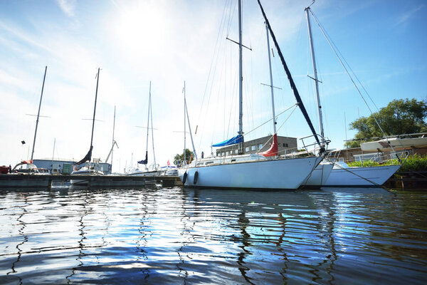 White sloop rigged yacht moored to a pier, a view from the water. Clear blue sky. Daugava river, port of Riga, Latvia