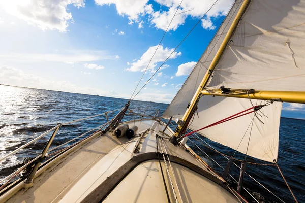 Sloop rigged yacht sailing on a clear day. A view from the deck to the bow and sails. Waves and water splashes. Baltic sea, Latvia