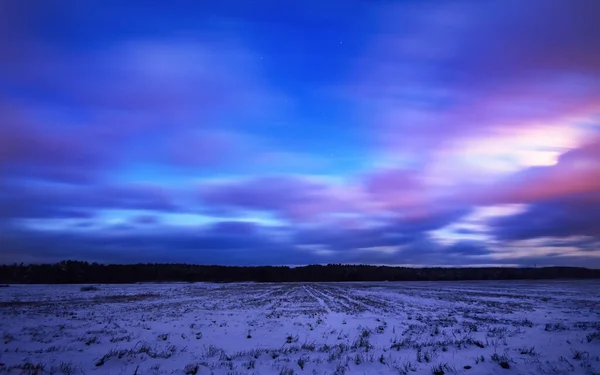 冬の風景 雪の夜にフィールドを介してカントリーロード覆われた 背景の森 カラフルな雲と素晴らしい夕日の空 ラトビア — ストック写真