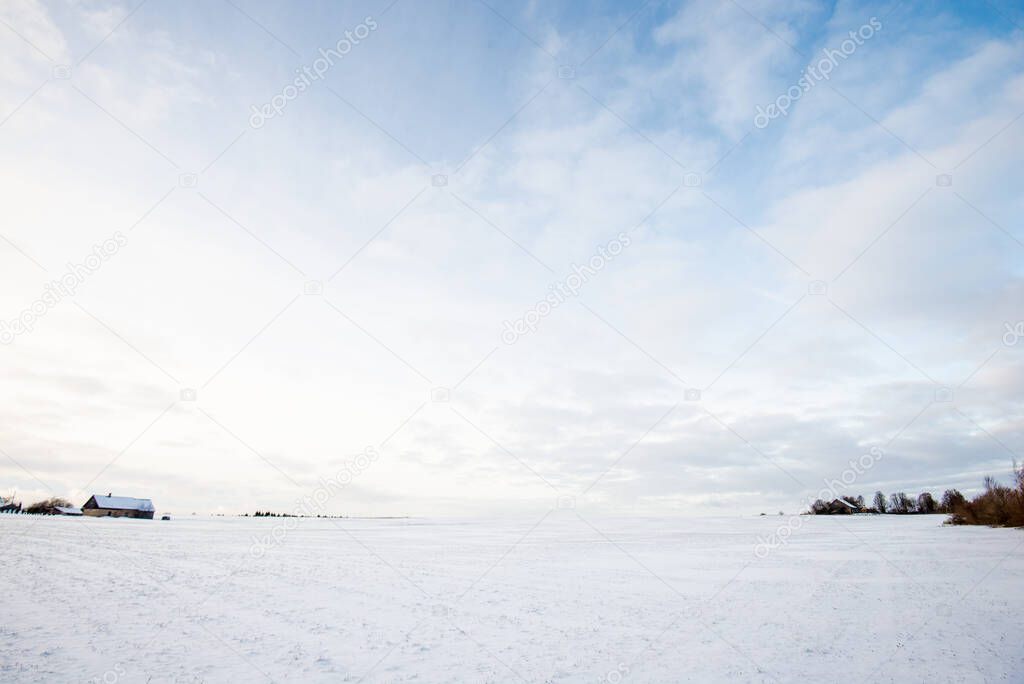 Panoramic view of the empty snow-covered country field at sunset. Evening clouds. Norway