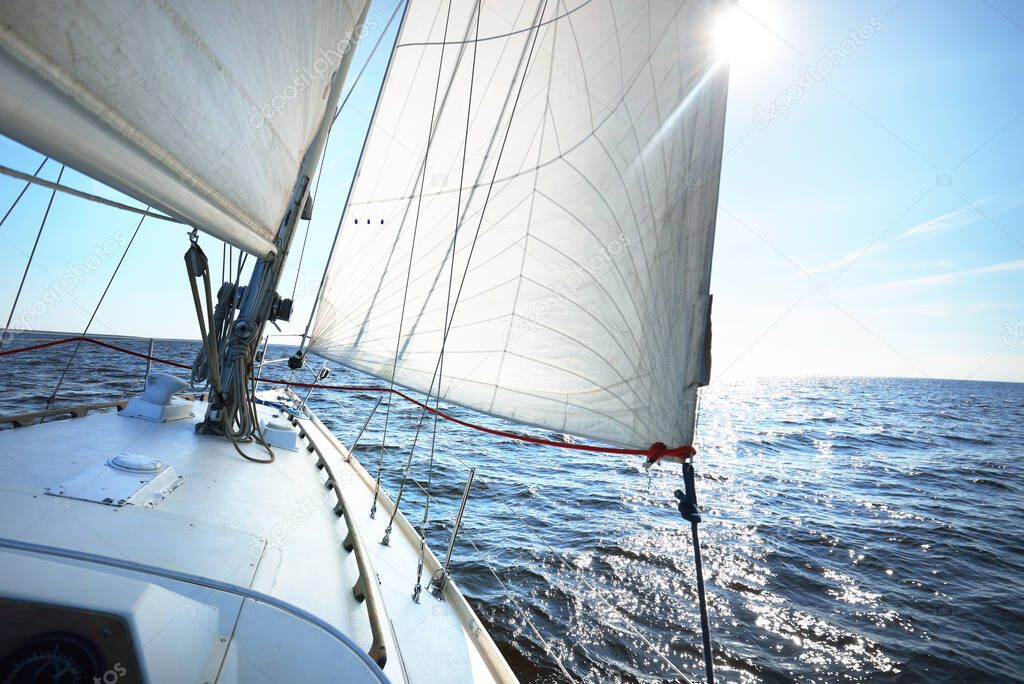 White sloop rigged yacht sailing in an open Baltic sea on a clear sunny day. A view from the deck to the bow, mast and sails. Estonia