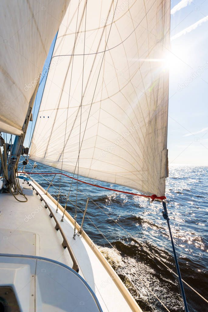 White sloop rigged yacht sailing in an open Baltic sea on a clear sunny day. A view from the deck to the bow, mast and sails. Waves and water splashes. Estonia