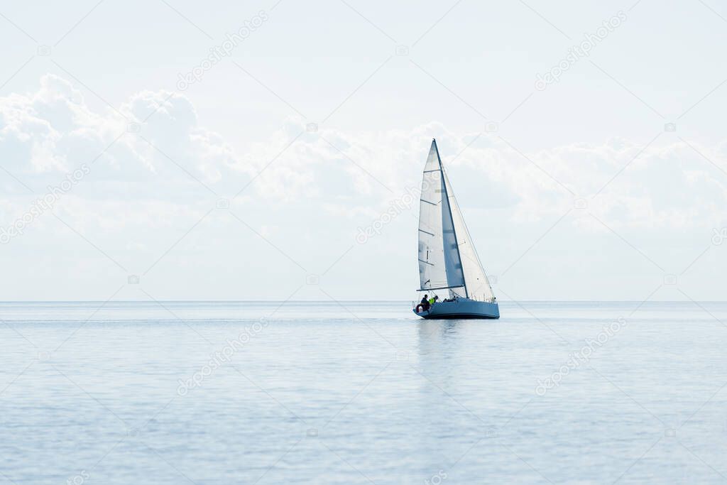 White sloop rigged modern yacht sailing in a Mediterranean sea on a clear sunny day, Spain. Blue sky with white clouds, reflections on water;