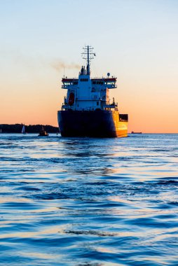 Gün batımında büyük bir kargo gemisi, yakın plan. Arka planda deniz feneri var. Riga, Letonya