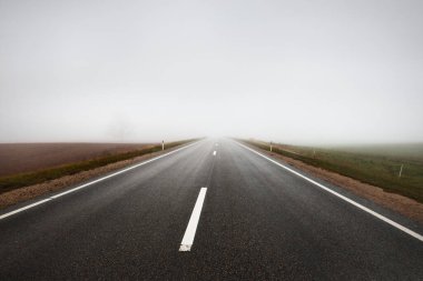 Kır manzarası. Güçlü bir sabah sisinin içinde boş bir asfalt yol. Orman ve arka planda evler. Polonya