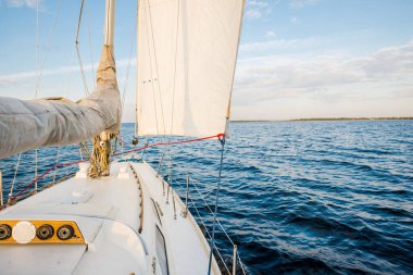 Gün batımında durgun suda yüzen beyaz bir yat. Güverteden pruvaya, direğe ve yelkenlere bir manzara. Şaşırtıcı bulut manzarası. Doğal ayna. Spor ve eğlence teması. Baltık Denizi, Letonya