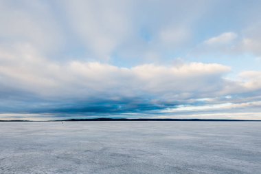 Kış manzarası. Gün batımında donmuş karla kaplı göl manzarası. Arka planda orman var. Renkli akşam bulutları. Onega Gölü, Karelia, Rusya
