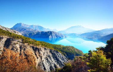 Güneşli bir günde Fransız Alplerindeki dağ gölü Lac de Serre-poncon 'un panoramik manzarası. Açık mavi gökyüzü, durgun su. Seyahat yerleri, turizm, dönüm noktası, doğa, Fransa 'da Noel tatilleri