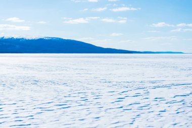 Donmuş gölün panoramik manzarası. Arka planda karla kaplı dağlar ve kozalaklı ormanlar var. Açık mavi gökyüzü. Kola Yarımadası, Murmansk bölgesi, Kutup Dairesi, Karelia, Rusya