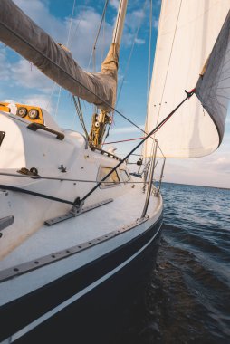 Mavi yat gün batımında Norveç 'te nehirde yüzüyor. Güverteden pruvaya ve yelkenlere bir manzara. Açık mavi gökyüzü. Spor ve eğlence teması