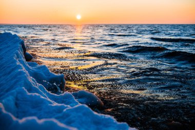 Renkli gün batımı. Güneşli bir kış gününde, karla kaplı deniz kıyısında. Letonya, Baltık Denizi üzerinde soğuk dalgalar