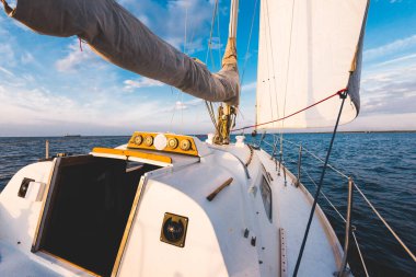 Gün batımında durgun suda yüzen beyaz bir yat. Güverteden pruvaya, direğe ve yelkenlere bir manzara. Şaşırtıcı bulut manzarası. Doğal ayna. Spor ve eğlence teması. Baltık Denizi, Letonya