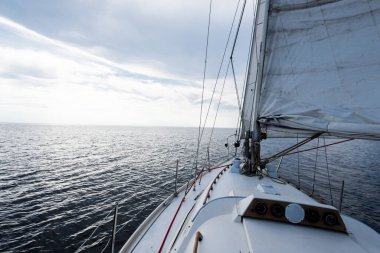 ABD 'nin güneybatı limanında, Maine kıyısında beyaz yelkenli yelkenli yelkenli. Güverteden pruvaya, direğe ve yelkenlere bir manzara. Koyu mavi fırtına gökyüzü, güneş bulutların arasından ışıldıyor
