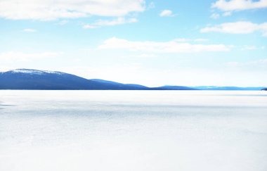 Donmuş gölün panoramik manzarası. Arka planda karla kaplı dağlar ve kozalaklı ormanlar var. Açık mavi gökyüzü. Kola Yarımadası, Murmansk bölgesi, Kutup Dairesi, Karelia, Rusya