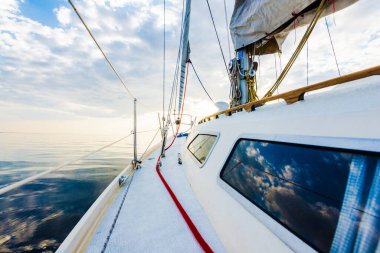 Gün batımında durgun suda yüzen beyaz bir yat. Güverteden pruvaya, direğe ve yelkenlere bir manzara. Şaşırtıcı bulut manzarası. Doğal ayna. Spor ve eğlence teması. Baltık Denizi, Letonya