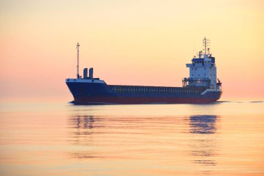 Gün batımında büyük bir kargo gemisi. Renkli akşam bulutları ve parlak güneş ışığı. Baltık Denizi, Letonya