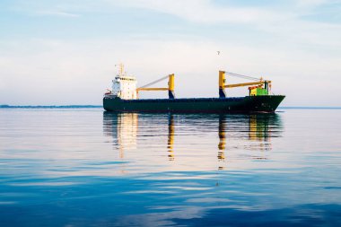 Gün batımında büyük bir yük vinci gemisi. Akşam bulutları ve parlak güneş ışığı. Baltık Denizi, Letonya